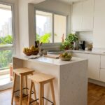 Banqueta para cozinha americana de madeira com apoio de pés, posicionada sob balcão de apartamento brasileiro